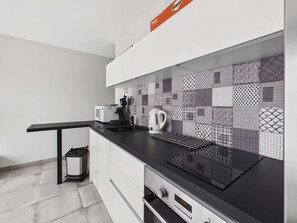 A modern kitchen with a black countertop, white cabinets, and patterned backsplash tiles. - Cozy apartment, south terrace - 4 guests (Marseillan-Plage)