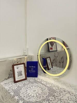 Um código QR emoldurado, um livro azul intitulado 'Un livre sur les fleurs' e um espelho redondo com moldura amarela sobre uma mesa estampada.