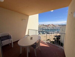 Un balcón con mesa y sillas, vista a un puerto deportivo y suelo de baldosas.