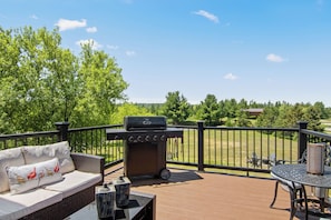 Una terraza con parrilla, mobiliario exterior y vistas a un paisaje verde.