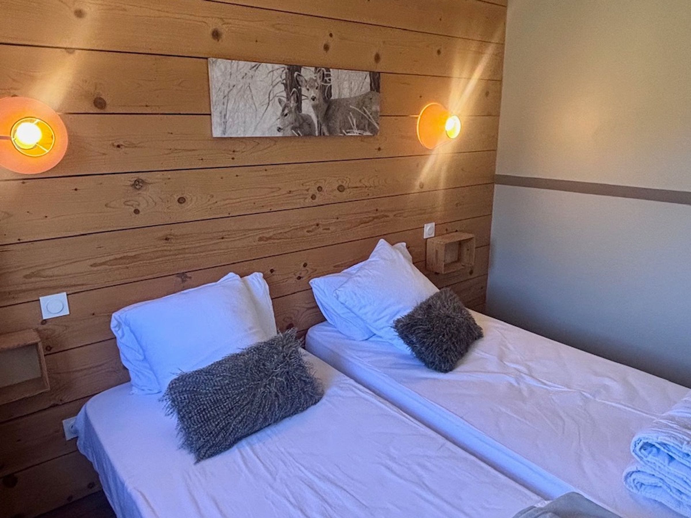 Una habitación con dos camas, paredes de madera y un cuadro de ciervos.