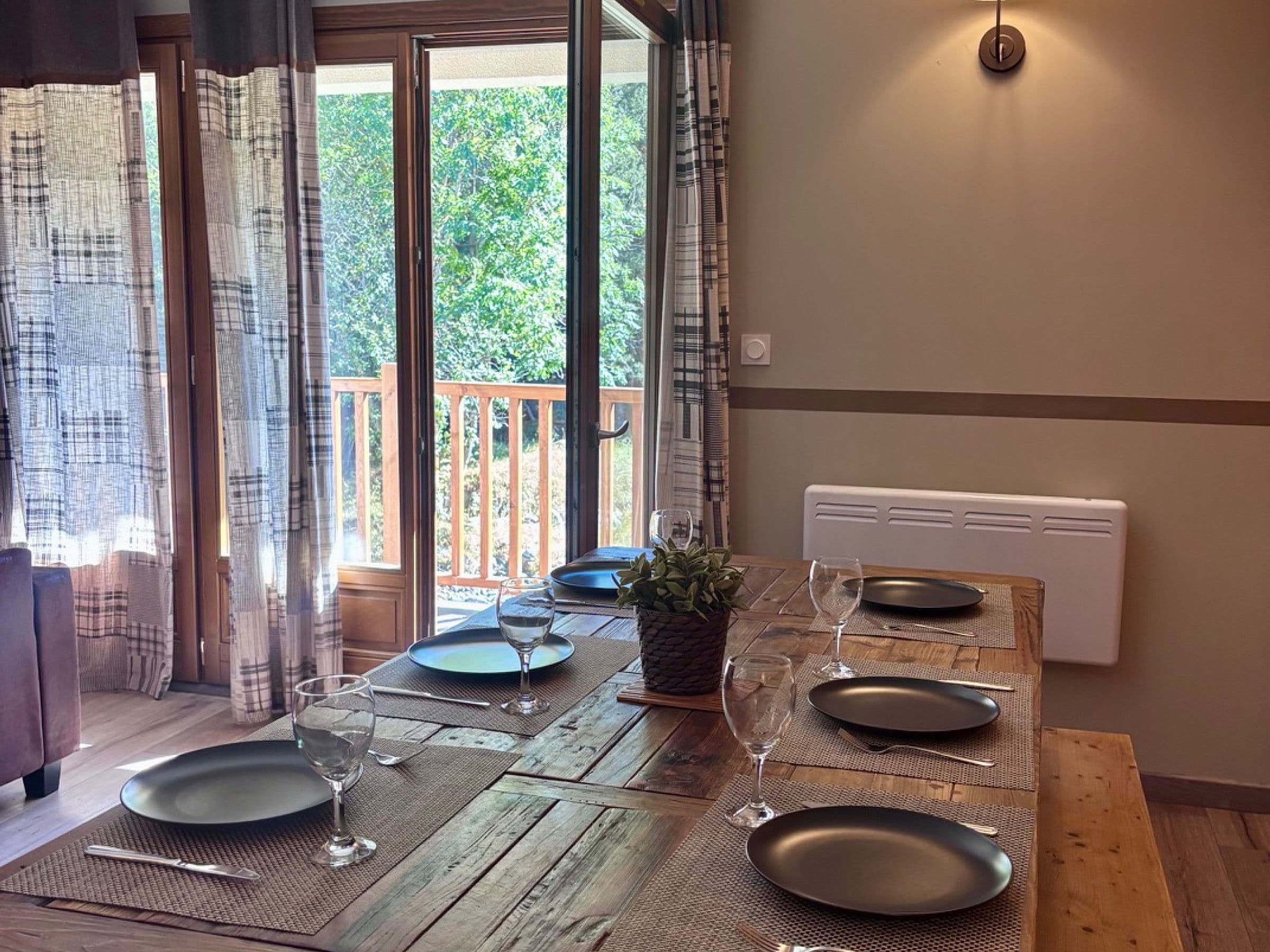 A dining table set for four with a view of a wooden deck and greenery outside.