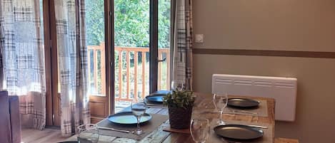 Une table à manger dressée pour quatre personnes, avec vue sur une terrasse en bois et la verdure environnante.