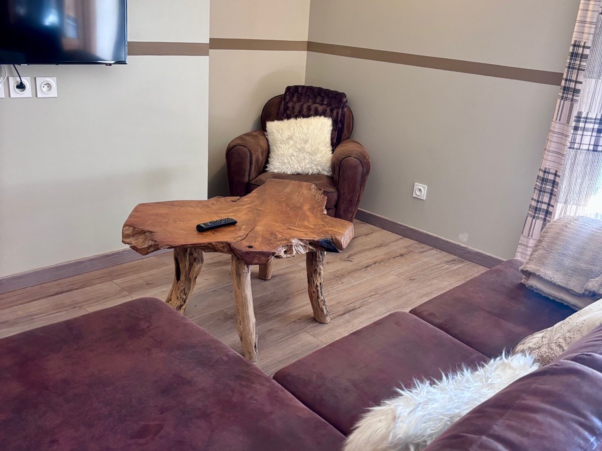 Un salon avec un canapé marron, une table basse en bois et un téléviseur fixé au mur.