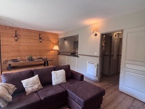 Ein modernes Wohnzimmer mit einem braunen Sofa, einem Esstisch für zwei Personen und einer Küchenzeile mit Kühlschrank und Schränken.