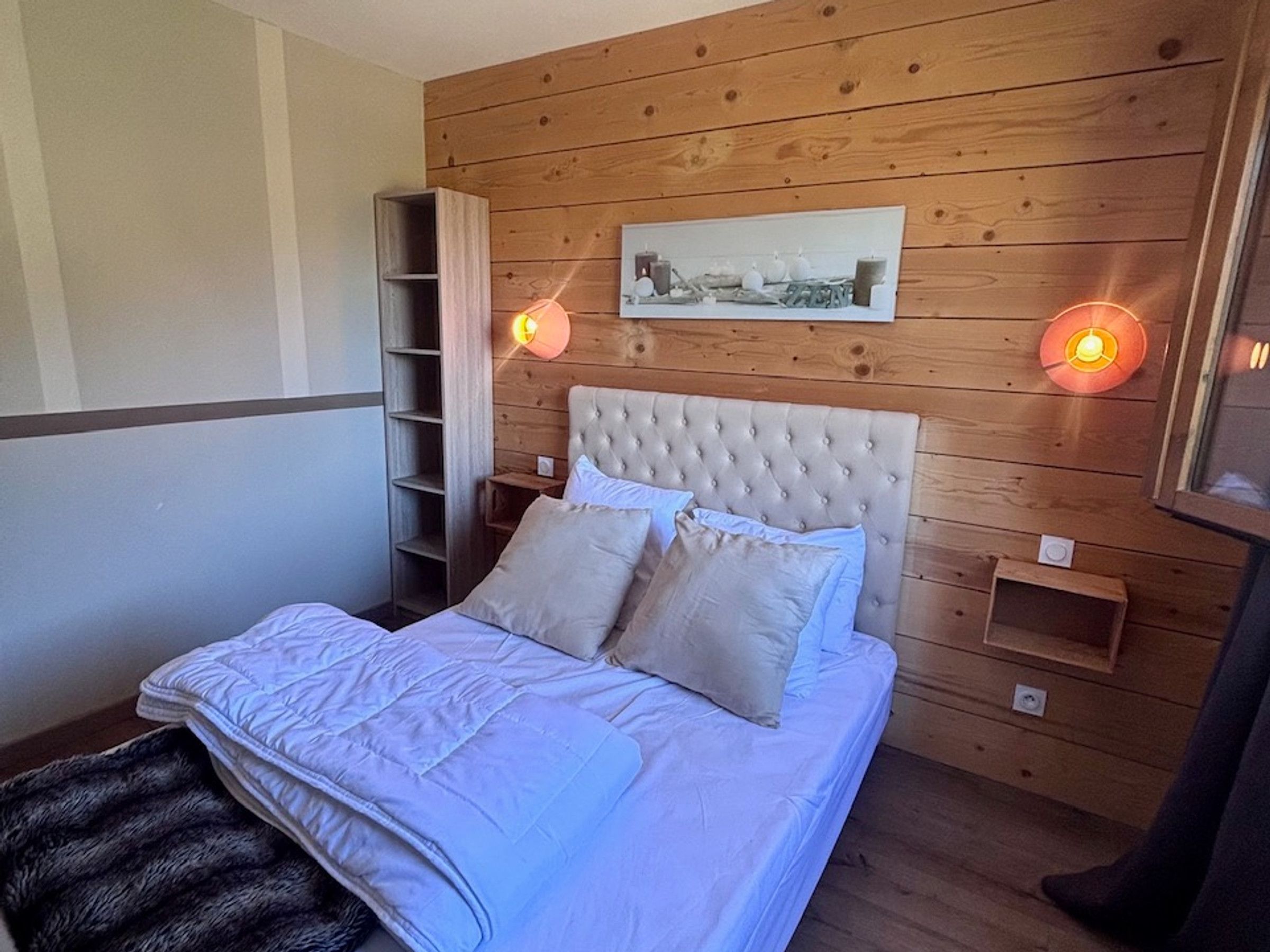 Une chambre à coucher avec une tête de lit en bois, un lit avec une literie blanche, une table de chevet et une étagère fixée au mur.