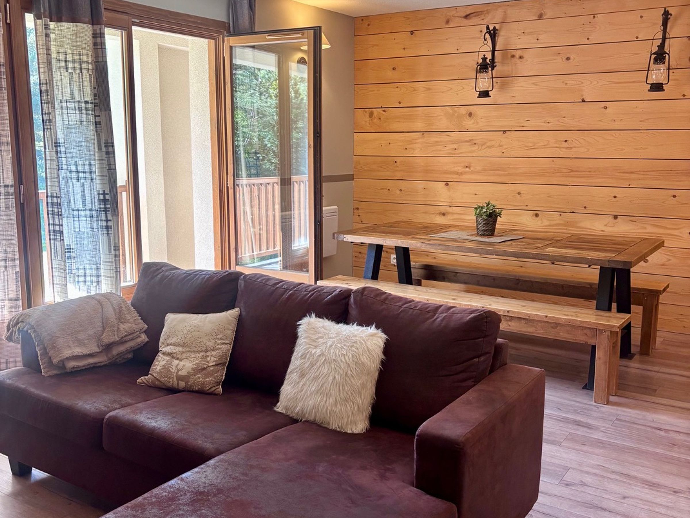 Una sala de estar acogedora con un sofá de cuero marrón, una mesa de comedor de madera con bancos y una pared de madera decorada con faroles colgantes.
