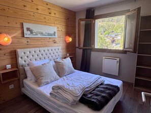 Ein Schlafzimmer mit einem hölzernen Kopfende, einem Bett mit weißen Leinen, zwei Nachttischen, einem Fenster mit Blick und einer Heizung.