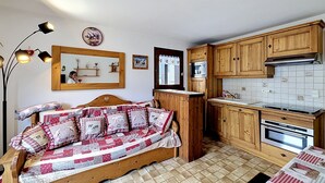 Ein gemütliches Zimmer mit einem Bett, einer hölzernen Bank, einer Küche mit Holzschränken, einer Mikrowelle und einem Herd.