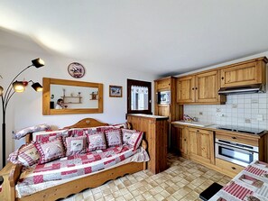 A cozy room with a bed, a wooden bench, a kitchen with wooden cabinets, a microwave, and a stove. - Charming apartment in Combloux center - 4 guests (Combloux)