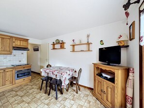 A kitchen with wooden cabinets, a tiled backsplash, a dining table with chairs, and a television on a wooden stand. - Charming apartment in Combloux center - 4 guests (Combloux)