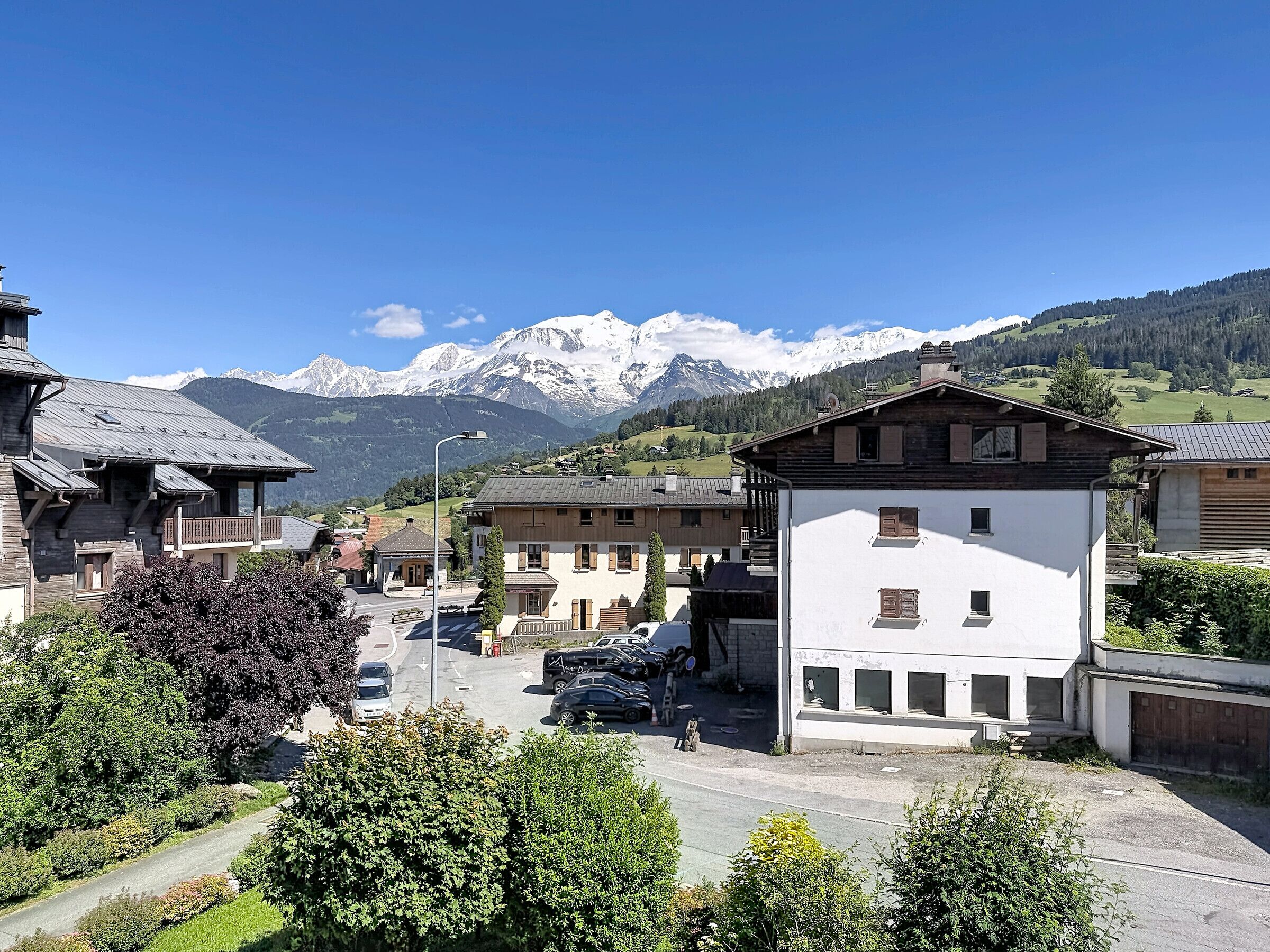 Ein Bergdorf mit traditionellen Holzhäusern, einer gepflasterten Straße und freiem Blick auf verschneite Berggipfel im Hintergrund.
