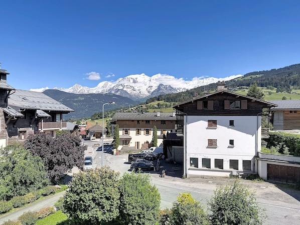 Ein Bergdorf mit traditionellen Holzhäusern, einer gepflasterten Straße und freiem Blick auf verschneite Berggipfel im Hintergrund.