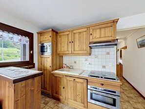 A kitchen with wooden cabinets, a microwave, a tiled backsplash, and a window with a view. - Charming apartment in Combloux center - 4 guests (Combloux)