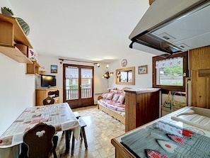 Ein gemütliches Zimmer mit Holztisch, einer Couch, einem Fernseher und einem Fenster mit Vorhängen.