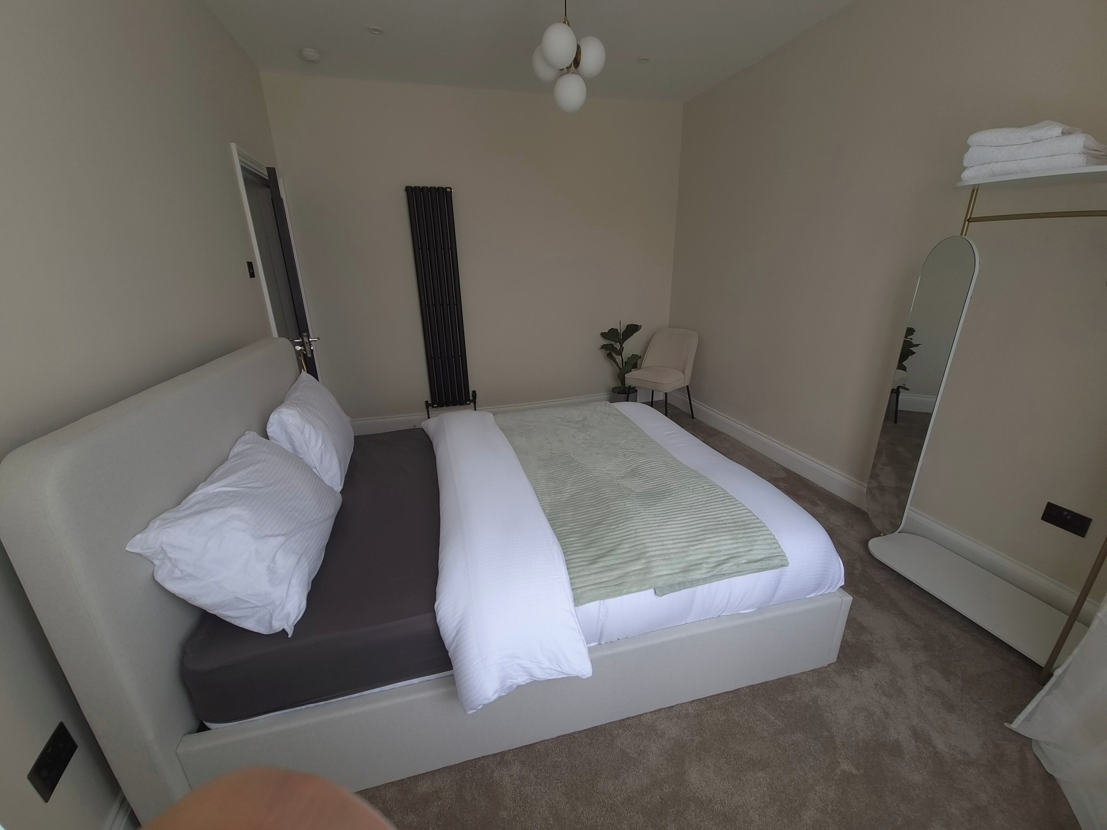 A bedroom with a bed, a radiator, a chair, a mirror, and a towel rack.