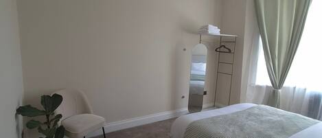 A bedroom with a bed, a chair, a dresser, a mirror, a ceiling fan, and a potted plant.