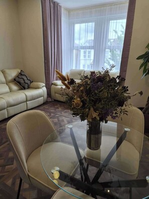 A living room with a glass table, beige sofa, and a vase with dried flowers. - Spacious Apartment Sleeps 2 With Parking, Newly Refurbished (Ilford)