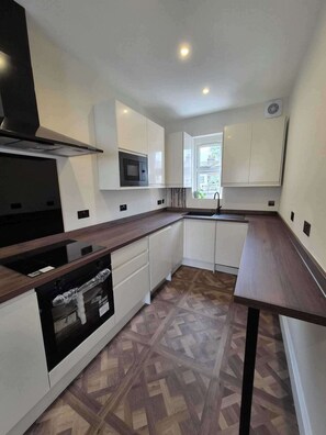 A modern kitchen with white cabinets, a microwave, a stove, and a window. - Spacious Apartment Sleeps 2 With Parking, Newly Refurbished (Ilford)