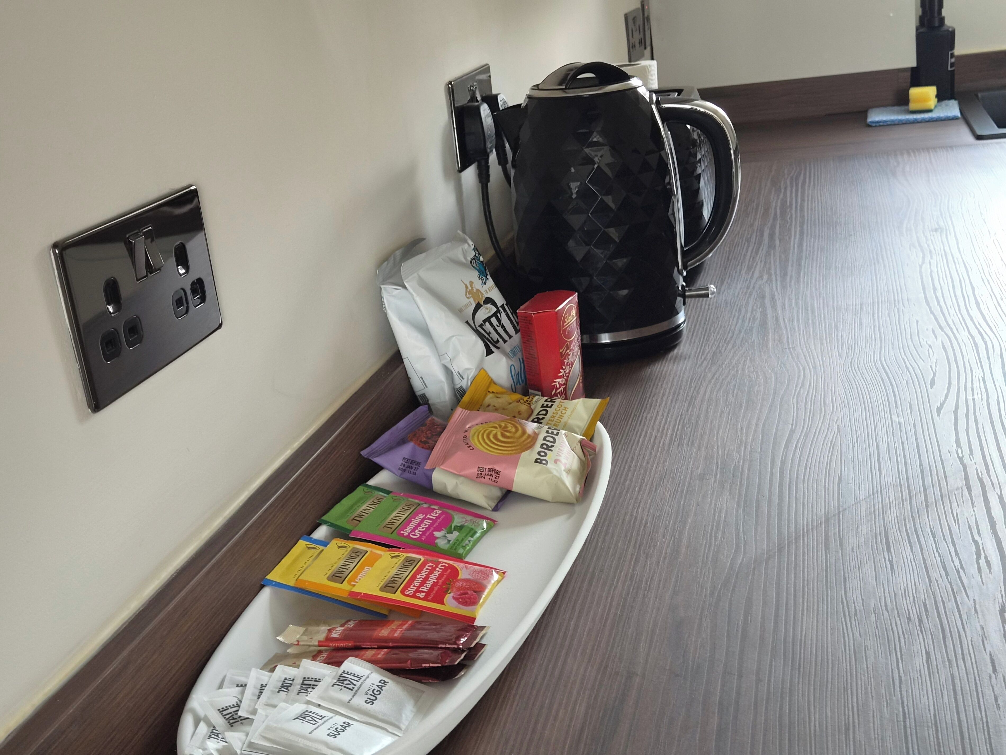 A tray with various food items and a kettle on a wooden floor.