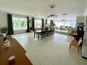 A spacious living area with a dining table, chairs, a piano, and a sofa.
