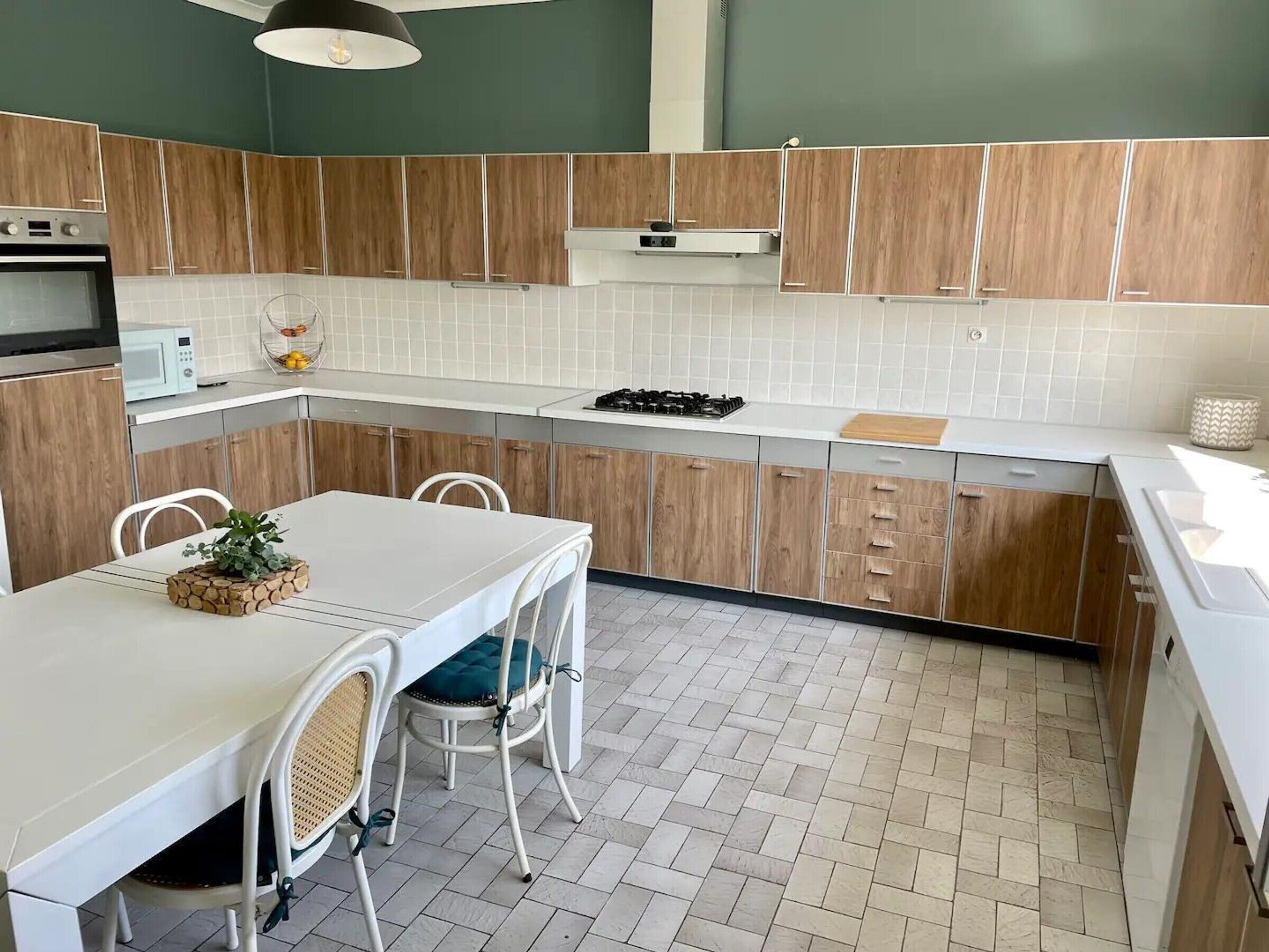 A modern kitchen with wooden cabinets, a white countertop, a dining table with chairs, and a microwave.