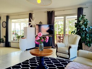 Un salon avec un tĂ©lĂ©viseur, une dĂ©coration en forme dâĂ©toile, un vase rempli de fleurs, un canapĂ© et une grande plante.
