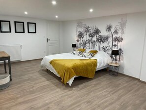 Une chambre à coucher comprenant un lit, deux tables de chevet, un radiateur et un mur orné d’une fresque aux motifs tropicaux.