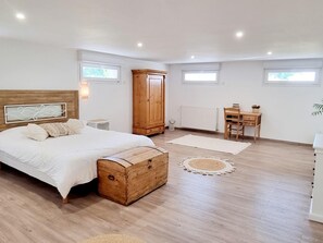 A bedroom with a bed, wooden chest, wardrobe, desk, chair, and a radiator.