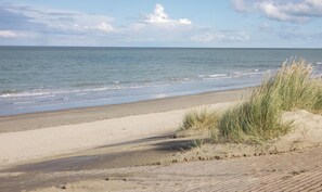 Une plage avec une promenade dallée, une rive sablonneuse et des dunes herbeuses.