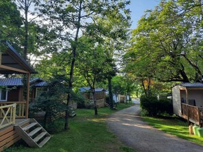 A row of wooden cabins with a gravel path leading through a wooded area. - Charming mobile home, terrace - 6 guests (Rocamadour)