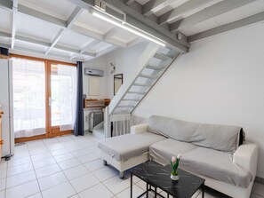Ein modernes Wohnzimmer mit einer Couch, einem kleinen Tisch, einer Heizung, einem Fenster mit Vorhängen, einer Treppe und einer Decke mit freiliegenden Balken.