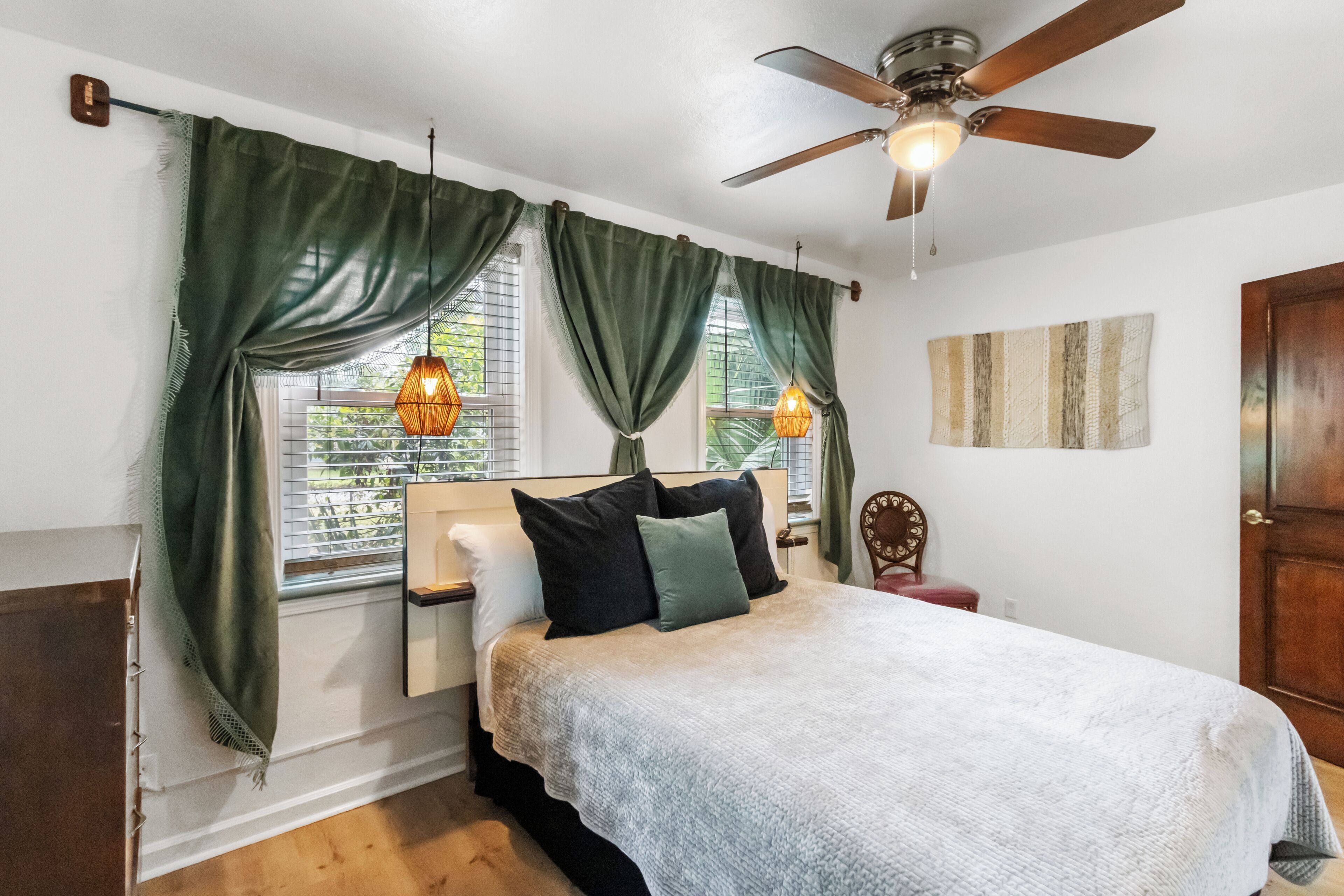 Un dormitorio con cama, cortinas, ventilador de techo y ventana con persianas.
