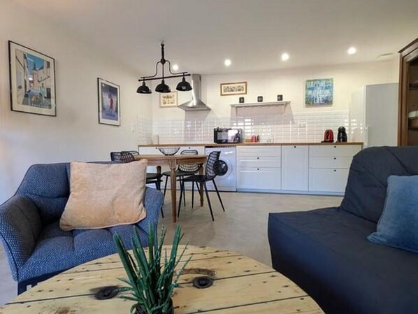 Ein modernes Wohnzimmer mit einer Couch, einem Couchtisch und einem Essbereich mit Stühlen sowie einer Küche im Hintergrund.