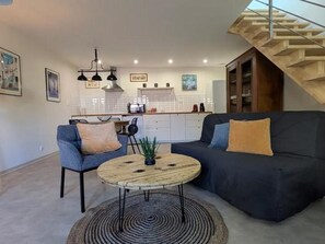 Ein modernes Wohnzimmer mit Sofa, Sesseln, einem Couchtisch und einer Treppe.
