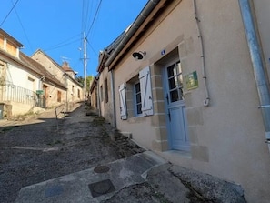 Une rue étroite bordée d’immeubles, une porte bleue et un couvercle de regard d’égout.
