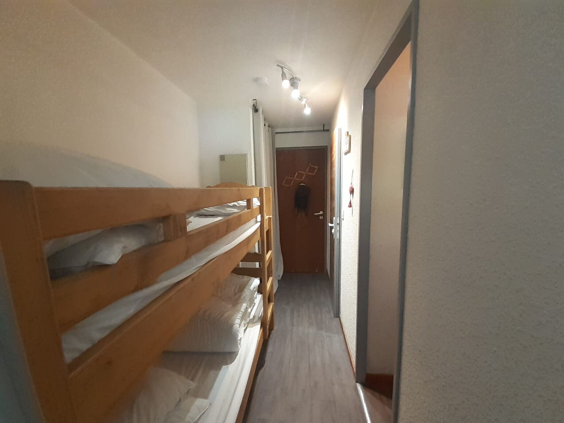 A narrow hallway with bunk beds on the left, a door at the end, and a light fixture above.