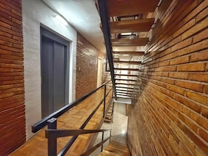 A corridor with brick walls, a wooden floor, and a metal railing.