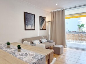 A modern living room with a wooden dining table, a sofa, and two framed artworks on the wall.