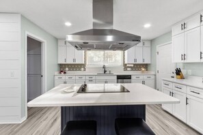A modern kitchen with white cabinetry, a central island, and a stainless steel range hood.