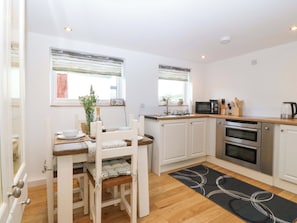 A compact kitchen with white cabinets, a microwave, and a double oven. - Ty Loti (Caernarfon)