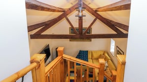 A wooden staircase with a railing leading to a room with a sofa and a television. - Ty Loti (Caernarfon)