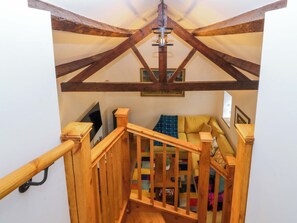 A wooden staircase with a railing leading to a room with a sofa and a television. - Ty Loti (Caernarfon)