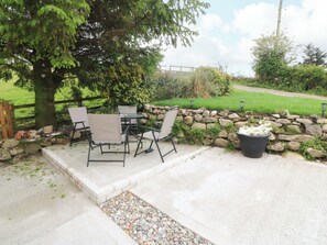An outdoor patio with a table and chairs, surrounded by a stone wall and greenery. - Ty Loti (Caernarfon)