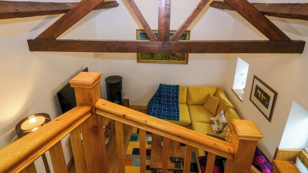 A wooden staircase with a wooden handrail, a ceiling light fixture, a sofa with patterned cushions, and a framed picture on the wall. - Ty Loti (Caernarfon)
