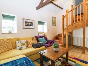A living room with a sofa, a wooden table, and a staircase. - Ty Loti (Caernarfon)