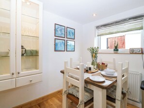 A dining area with a wooden table, white chairs, a radiator, and framed pictures on the wall. - Ty Loti (Caernarfon)