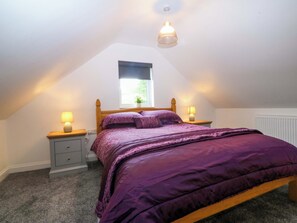 A bedroom with a bed, two bedside tables, a window, and a ceiling light. - Ty Loti (Caernarfon)