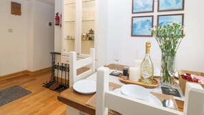 A dining area with a wooden table set for two, a bottle of Prosecco, a vase of flowers, and framed artwork on the wall. - Ty Loti (Caernarfon)