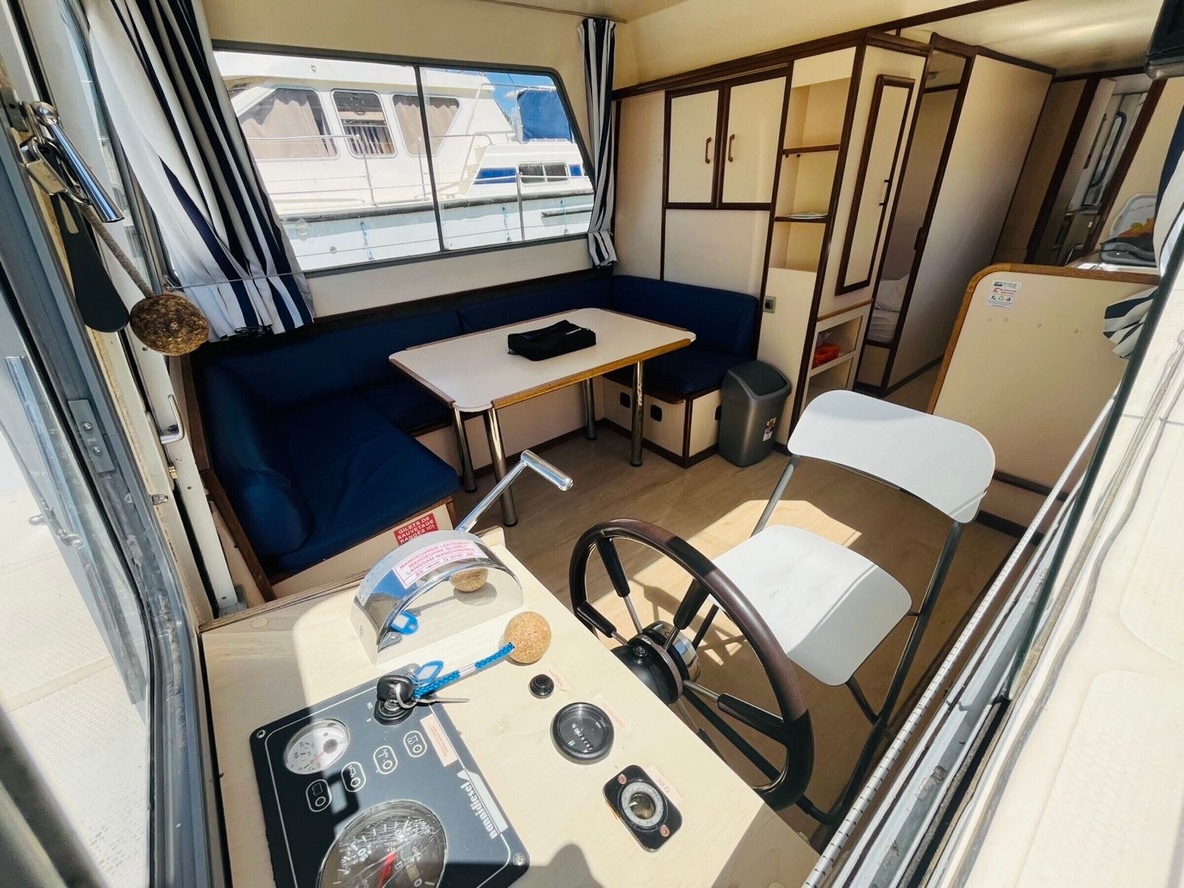 Een compact RV-interieur met een kitchenette, een zithoek met een tafel en een blauwe bank, een kleine witte stoel en een stuurconsole.